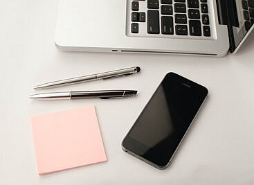 laptop, post-it pad, pens and iphone on a desk
